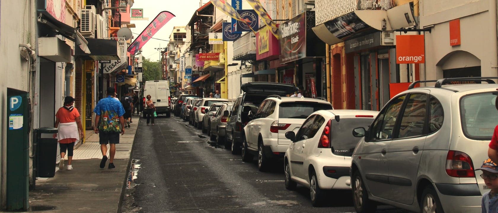 Rue commerçante du centre de Fort-de-France, voitures garées le long du trottoir et piétons sur la chaussée